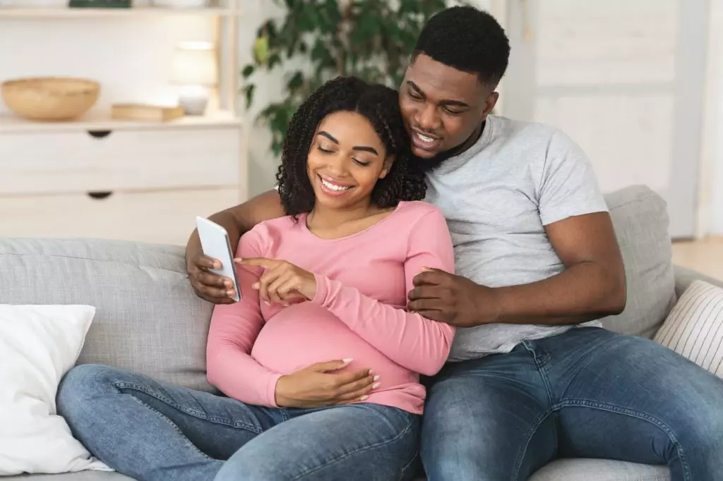 Pregnant black couple using smartphone together at home